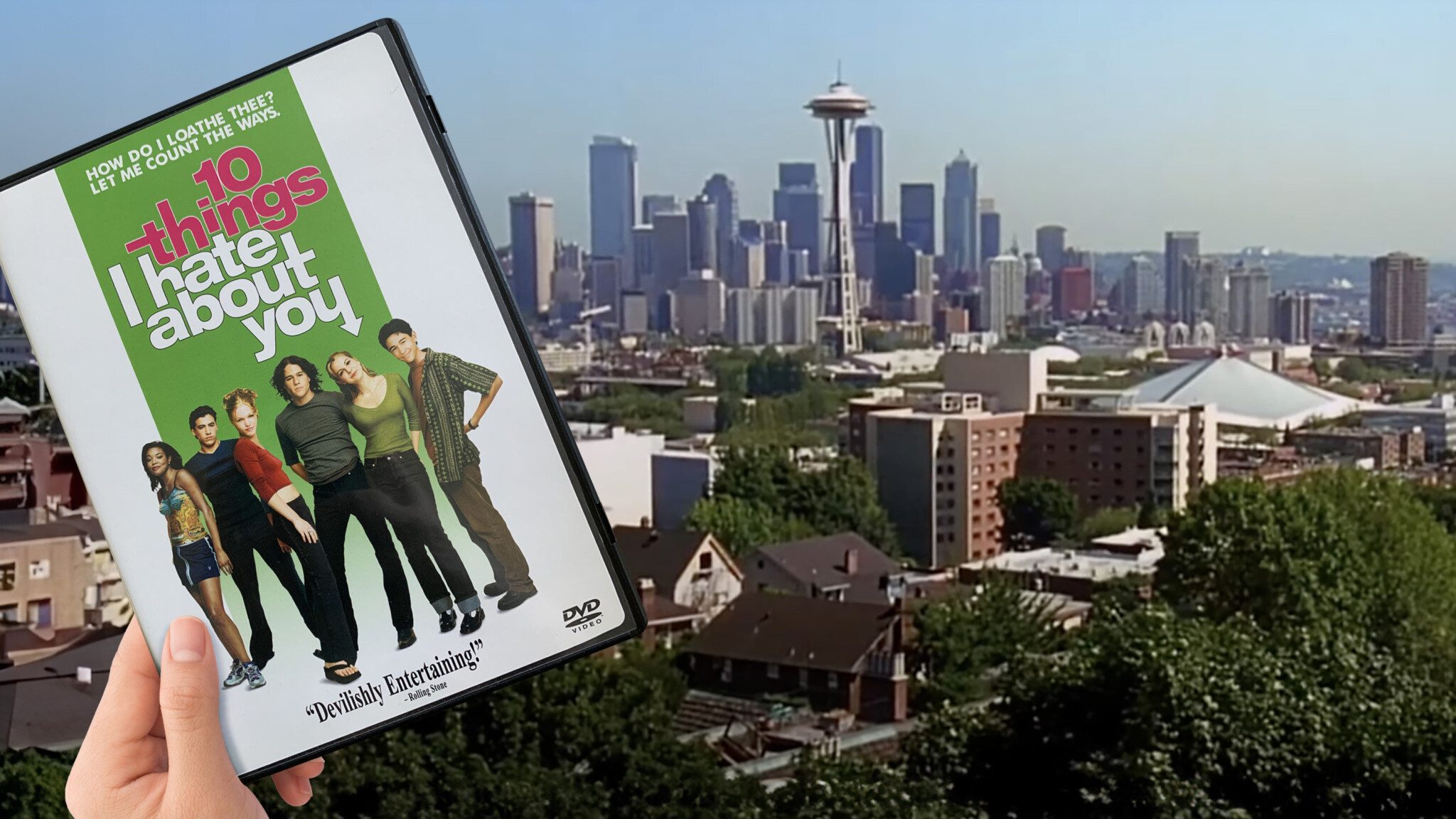 10ThingsIHateAboutYouDVDInSeattle_16x9 Hand holding a DVD of "10 Things I Hate About You" in front of a city skyline that matches the setting of the movie, celebrating its 25th anniversary.