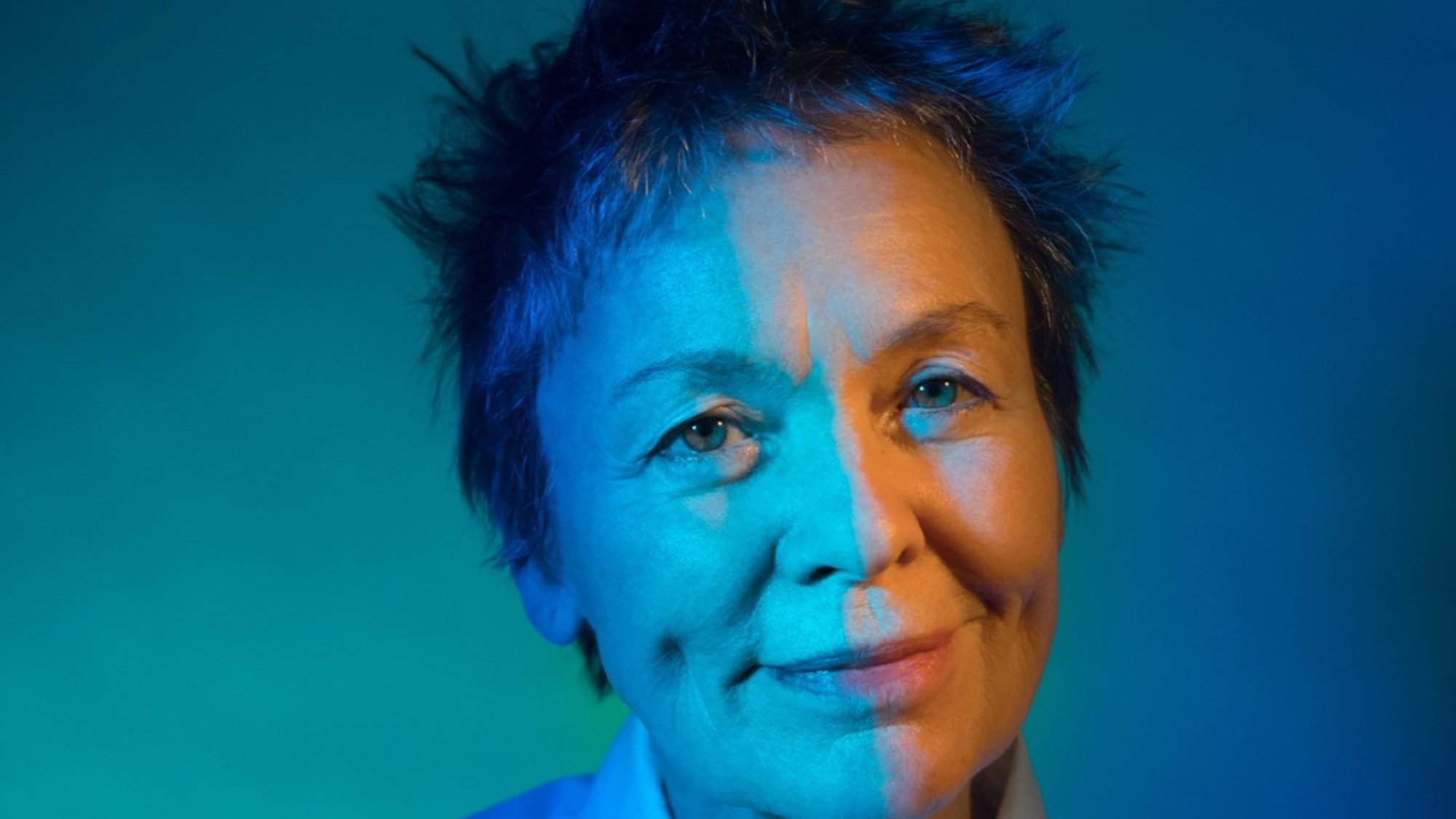 Portrait of Laurie Anderson with short hair against a blue-green gradient background.