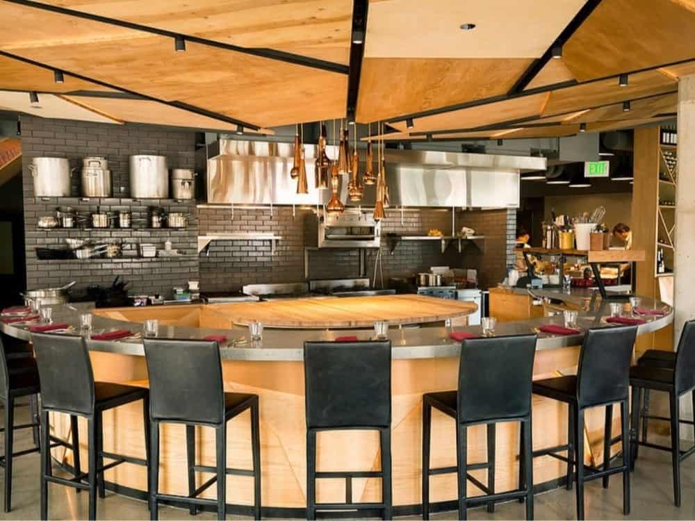 Art of the Cocktail-4-3-1000x750 Modern culinary retreat interior showing an open kitchen, bar stools in front, hanging copper pots, and a wooden ceiling.
