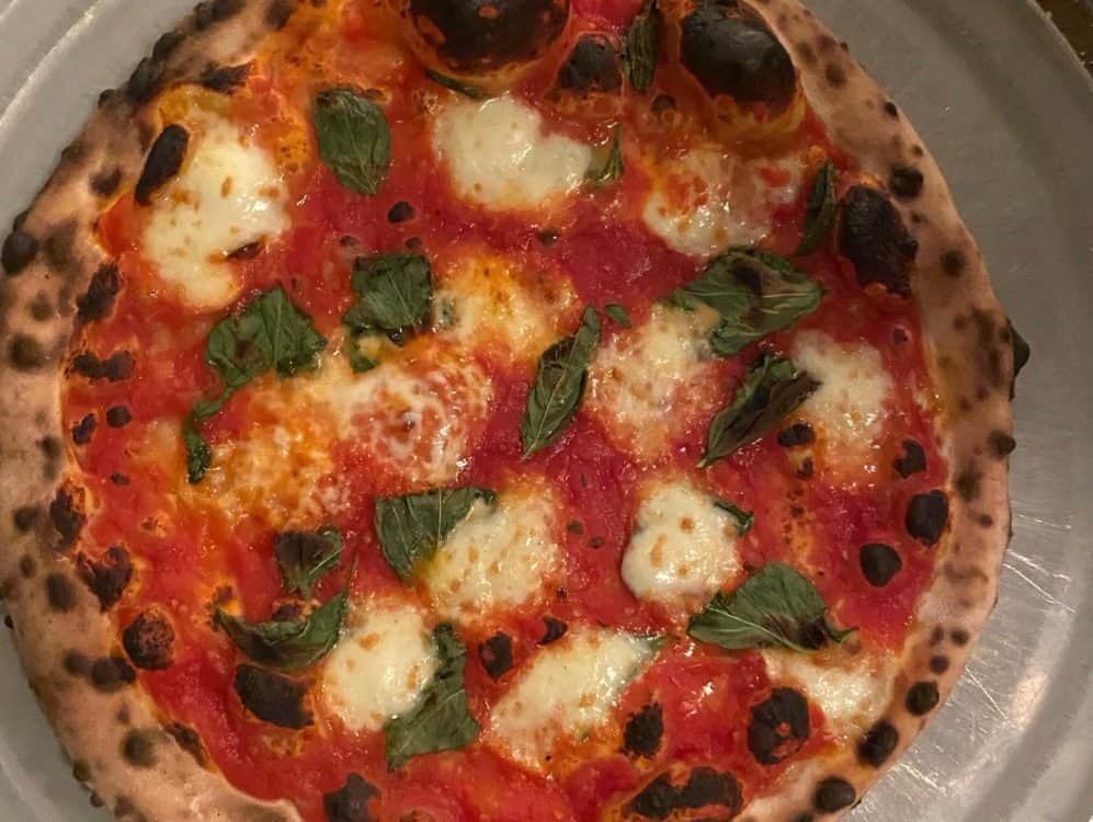 Delancey and Essex-4-3-1000x750 A freshly baked pizza with tomato sauce, melted mozzarella cheese, and basil leaves, featured in Seattle magazine, showing a well-charred crust.