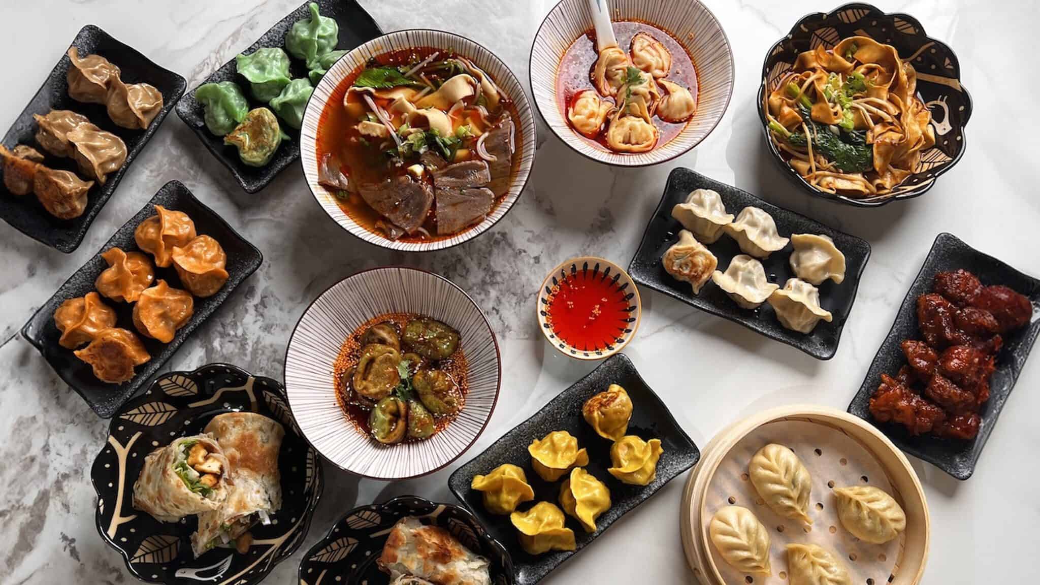 DumplingTheNoodle01_16x9 Assorted Asian dumplings and noodle dishes displayed on various patterned plates, with dipping sauces, featured during Seattle Restaurant Week, on a marble surface.