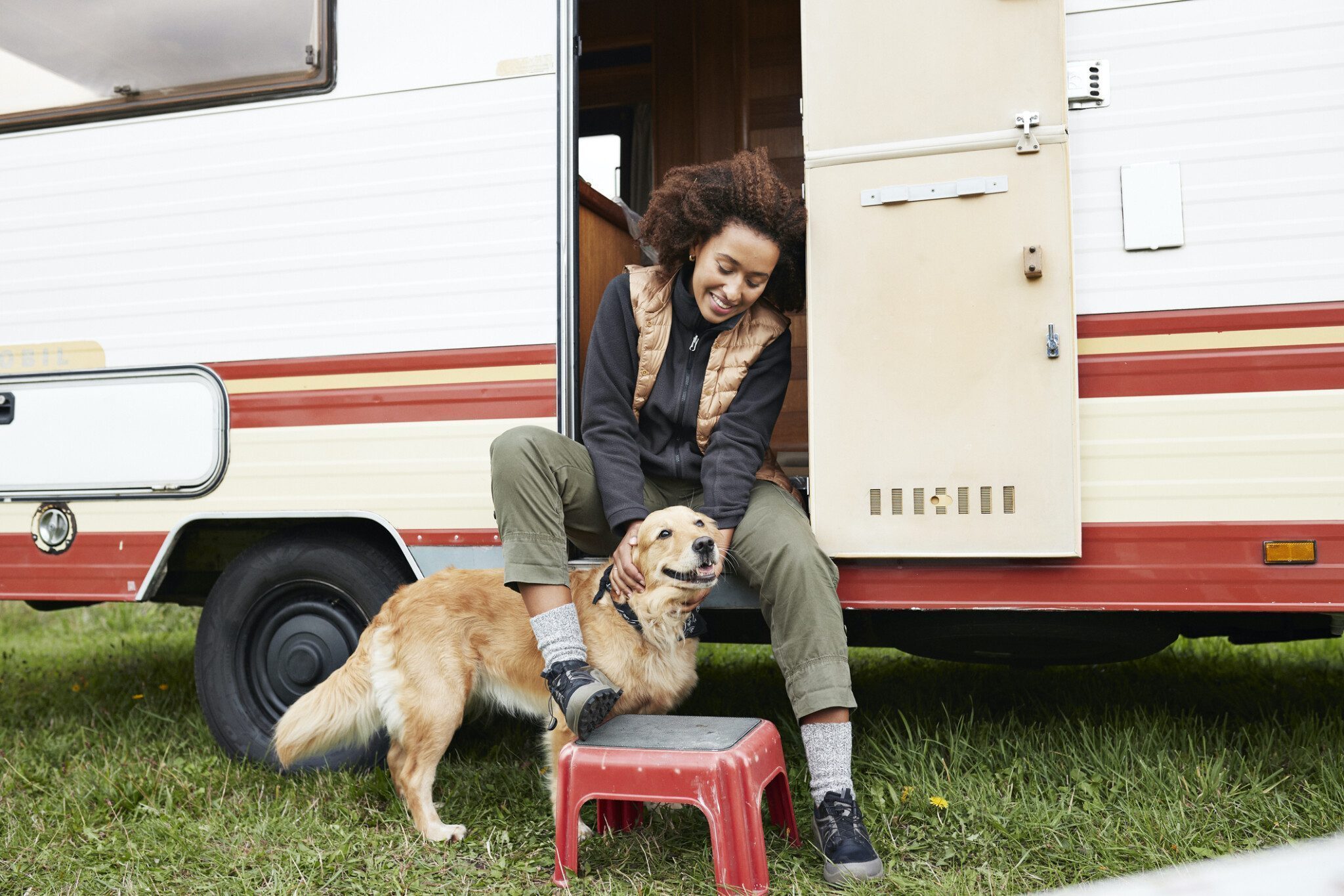 Woman sitting with dog on doorway of camper van Smiling woman sitting with dog on doorway of camper van during vacation