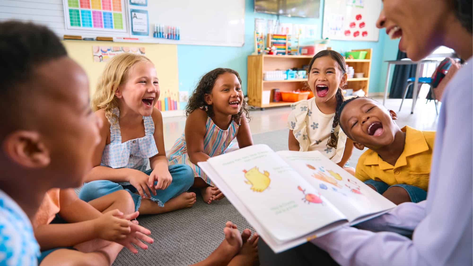GettyImages-2096525904-16-9-2000x1125 A group of children sit in a colorful, educational classroom, laughing, while a teacher reads a picture book to them. It's no wonder a report ranks Washington state No. 1 for teachers—this cheerful scene is a testament to their dedication and the vibrant learning environment they create.