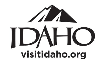 Logo of Iconic Idaho featuring stylized mountain peaks above the word "Idaho" and the website "visitidaho.org" below in black and white.