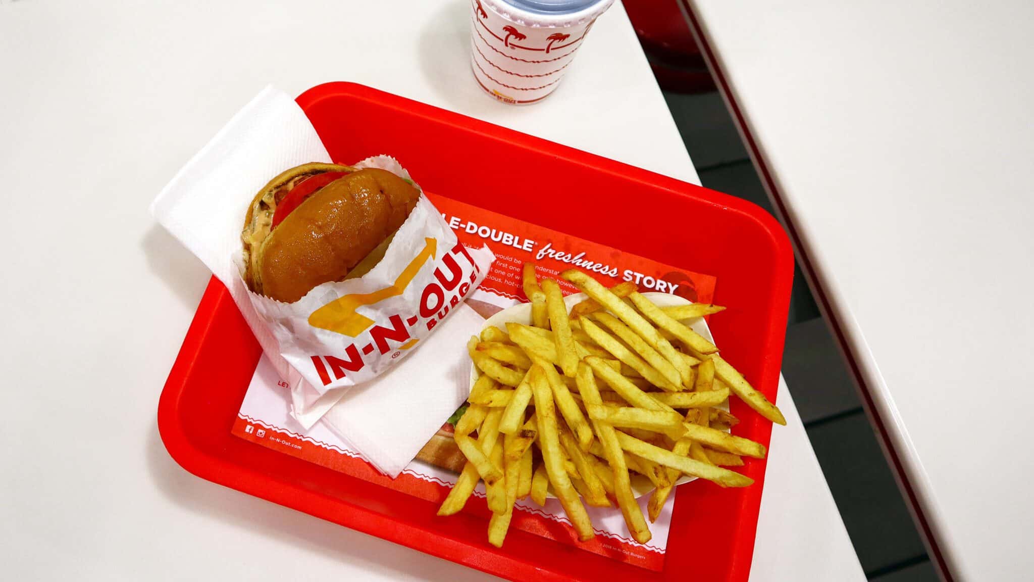 In-N-Out_16x9 A tray with an In-N-Out burger and fries on a red table, accompanied by a drink with the restaurant's logo.