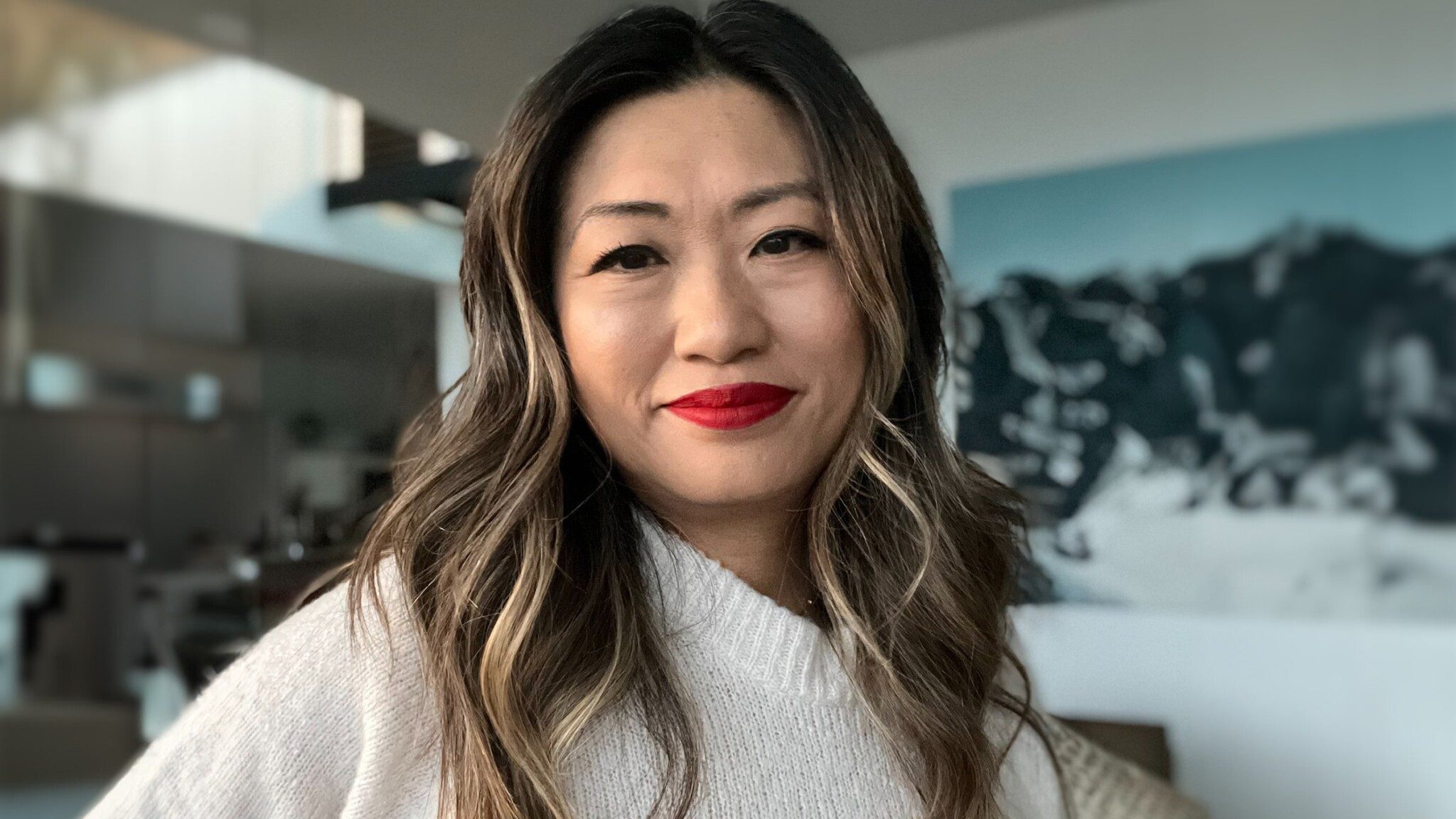 Jane-Park_16x9-min A woman with red lipstick smiling in a room with an art piece by Uncommon Thinkers in the background.