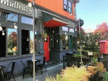Mulleady's Irish Pub Exterior of "mulleady's" pub with vibrant orange walls, hanging flower pots, outdoor seating, and string lights, featured in Seattle magazine.