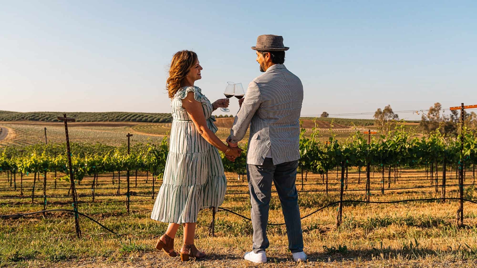 Photo 1-16-9-2000x1125-min Couple holding hands and toasting with wine in a hidden gem vineyard at sunset.
