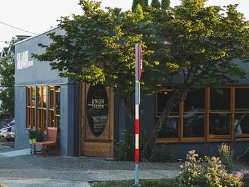 Union Saloon A cozy corner cafe with large windows and a green tree outside, named "Union Saloon," located in a quiet neighborhood, featured in Seattle Magazine.