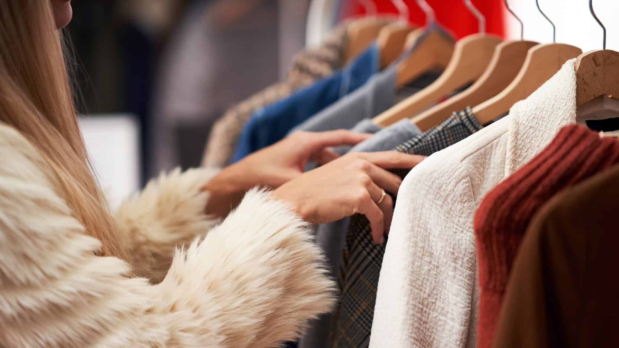 YourGuideToClosetRefresh_02_16x9 Two people browsing through a clothes rack in a store, examining various garments for a closet refresh.